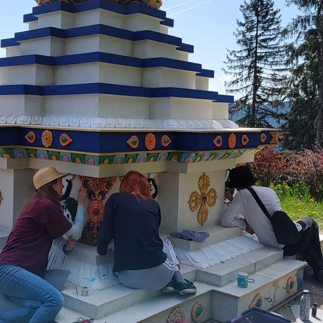 Dharma students volunteering to paint the stupa at Dzokden Kalap in Austria. They are adding blue paint and painting the details. 